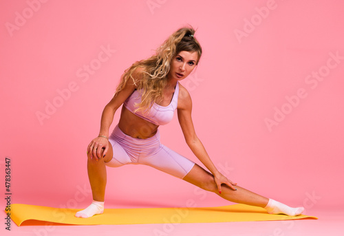 young athletic woman in tight clothes doing stretching on pink background