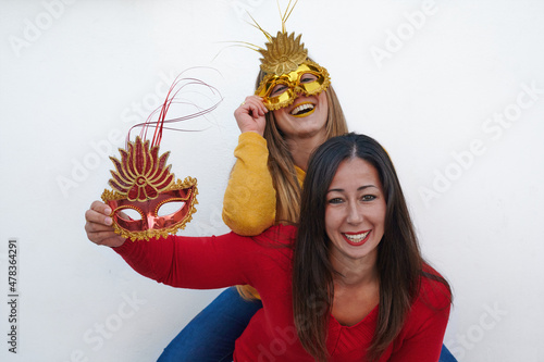 Fototapeta Naklejka Na Ścianę i Meble -  Two beautiful women wearing Venetian carnival masks and make-up laugh together over each other.