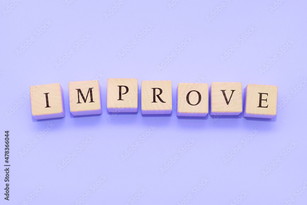 The word IMPROVE is made of wooden cubes on a violet background. The word IMPROVE is made of wooden cubes on a violet background.