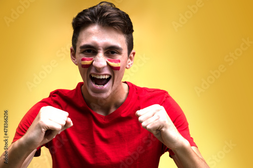 Spanish football fan happy for his national team, isolated on yellow background. Flag painted over face