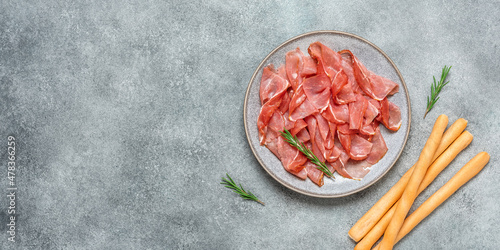 Slices of prosciutto di parma or jamon serrano in a plate and breadsticks on gray grunge background. Top view, flat lay, banner. photo