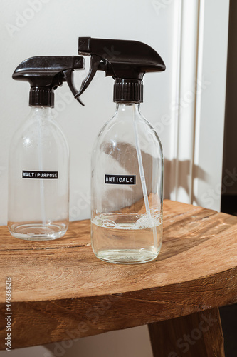 Two glass spray bottles anti-calc product on wooden surface on white wall background. Home made cleaning detergent recipe. Eco friendly zero waste household concept.