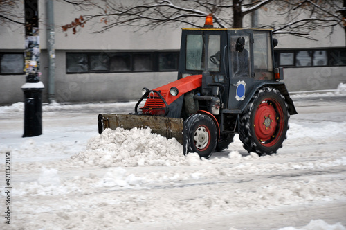 A snowblower removes snow in the city. A snow plow tractor shovels snow with a shovel. 
