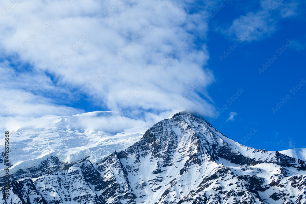 Mont Blanc and Aiguille du Gouter surrounded by clouds in Europe, France, the Alps, towards Chamonix, in summer, on a sunny day.