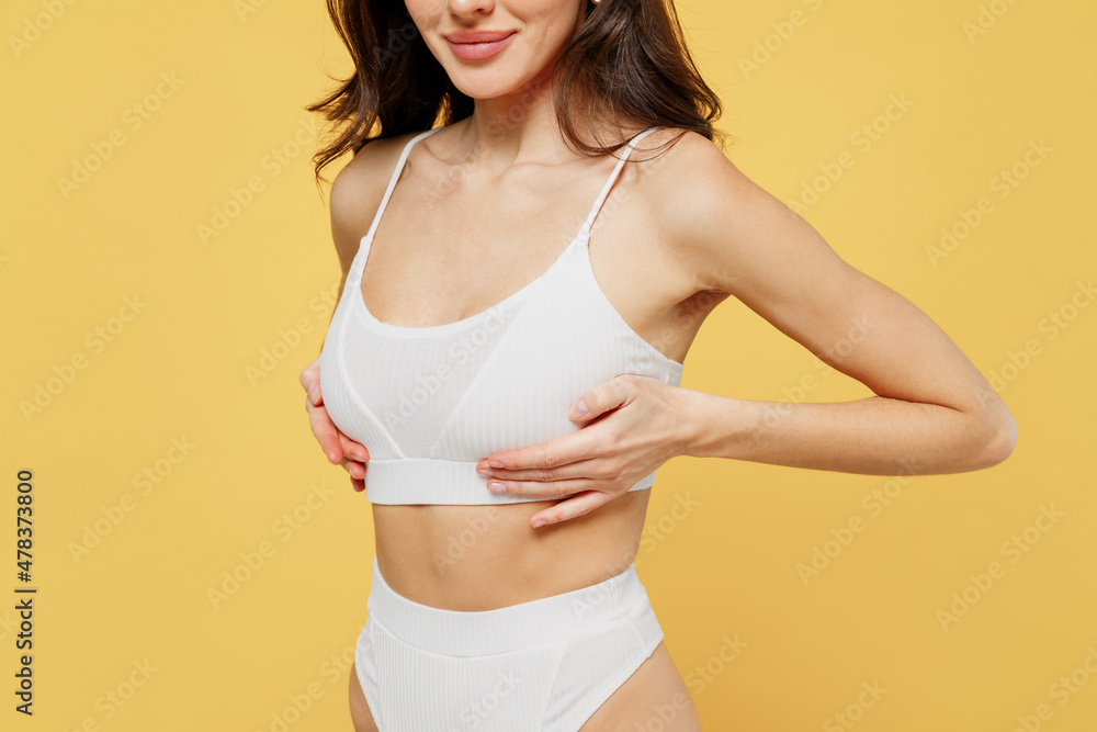 Cropped image side view of young woman 20s in white brassiere underwear put hand on chest breast cancer early diagnostic therapy treatment isolated on on plain yellow color background studio portrait. Cropped image side view of young woman 20s in white brassiere underwear put hand on chest breast cancer early diagnostic therapy treatment isolated on on plain yellow color background studio portrait.