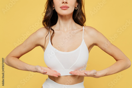 Cropped image of young woman 20s wear white brassiere underwear put hand on chest breast cancer early diagnostic therapy treatment isolated on on plain yellow background studio Augmentation concept photo