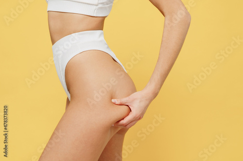 Cropped close up side view slim skinny caucasian young woman 20s in white underwear thong with perfect fit body show legs hips tweak buttocks isolated on plain yellow color background studio portrait.