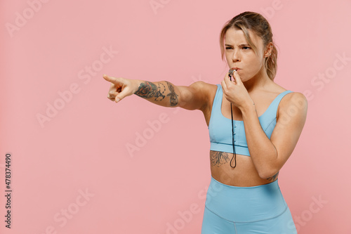 Schilderij op canvas Young strong sporty athletic fitness trainer instructor woman wear blue tracksuit spend time in home gym whistle point finger aside isolated on plain pink background