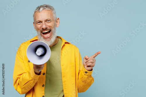 Elderly happy gray-haired mustache bearded man 50s in yellow shirt hold scream in megaphone announces discounts sale Hurry up point finger aside isolated on plain pastel light blue background studio