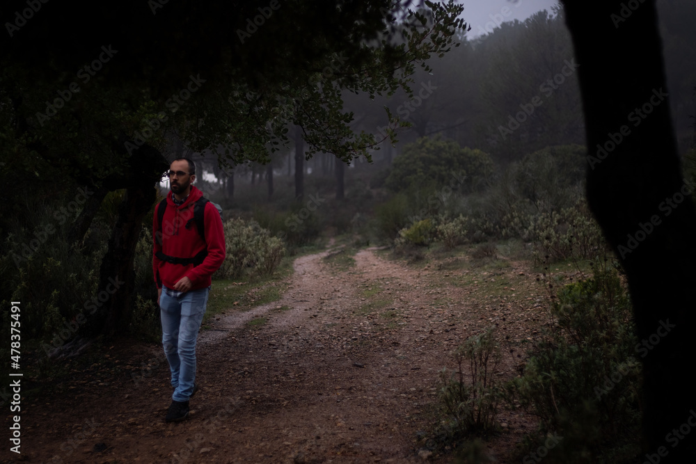 Hiker with red sweatshirt walking through the forest on a foggy day