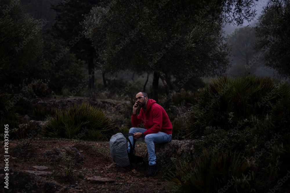 Hiker with red sweatshirt sitting on a stone in the forest on a foggy day