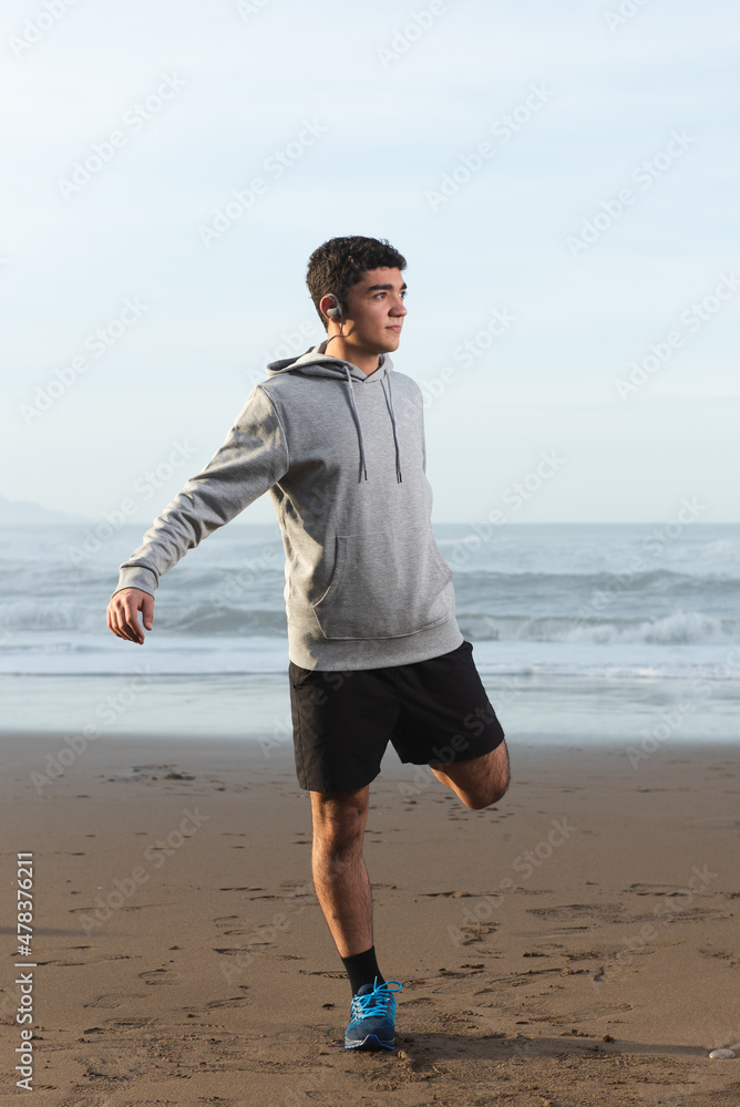 Hispanic teenager warming up before training at the beach Hispanic teenager warming up before training at the beach