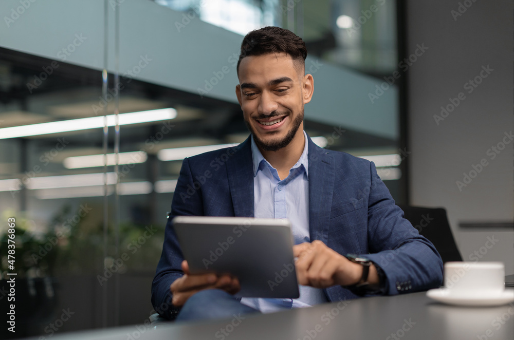 Cheerful middle eastern guy CEO working at office, using pad Cheerful middle eastern guy CEO working at office, using pad