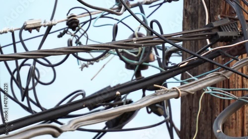 Black fiber optic cables for communication systems hung on the cables at the power poles, mess of tabgled cables and wires photo