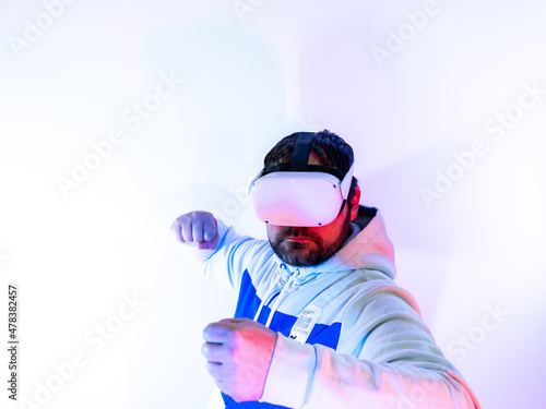 Young man wearing virtual reality headset playing in the metaverse - playing his beating with both fists - VR goggles