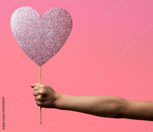 Hand of child holding pink shiny heart against pink background