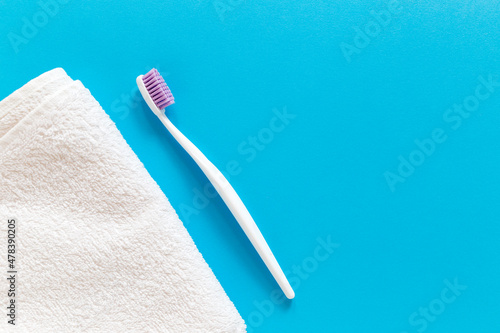 Flatlay of white towel and toothbrush on a blue background with copy space for your text. Morning routine and oral mouth and teeth hygiene concept