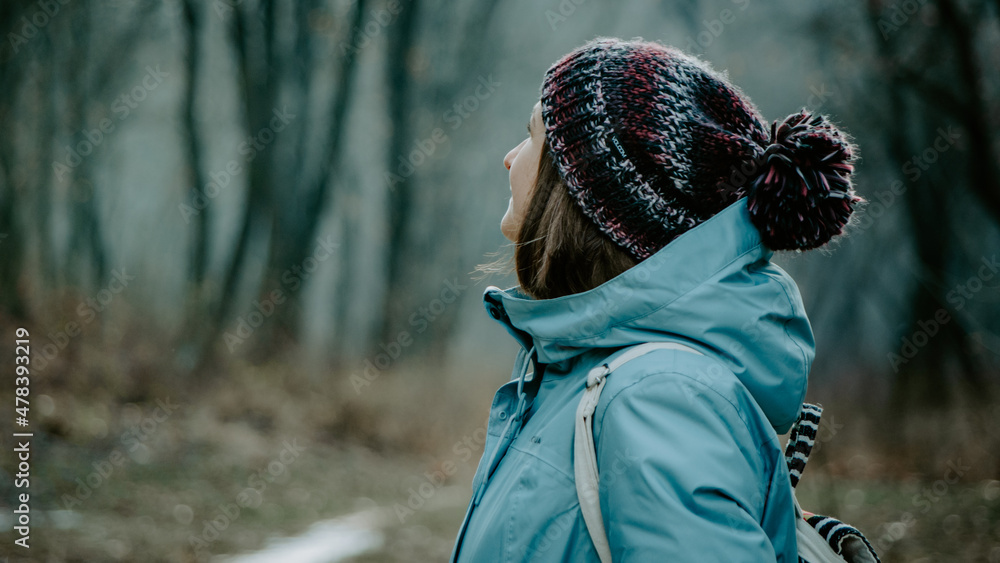 Cinematic side view of woman in a beanie and blue jacket wandering in the forest Cinematic side view of woman in a beanie and blue jacket wandering in the forest