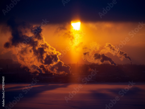 Chimneys of a factory with smoke and steam on a red sunset in the background.