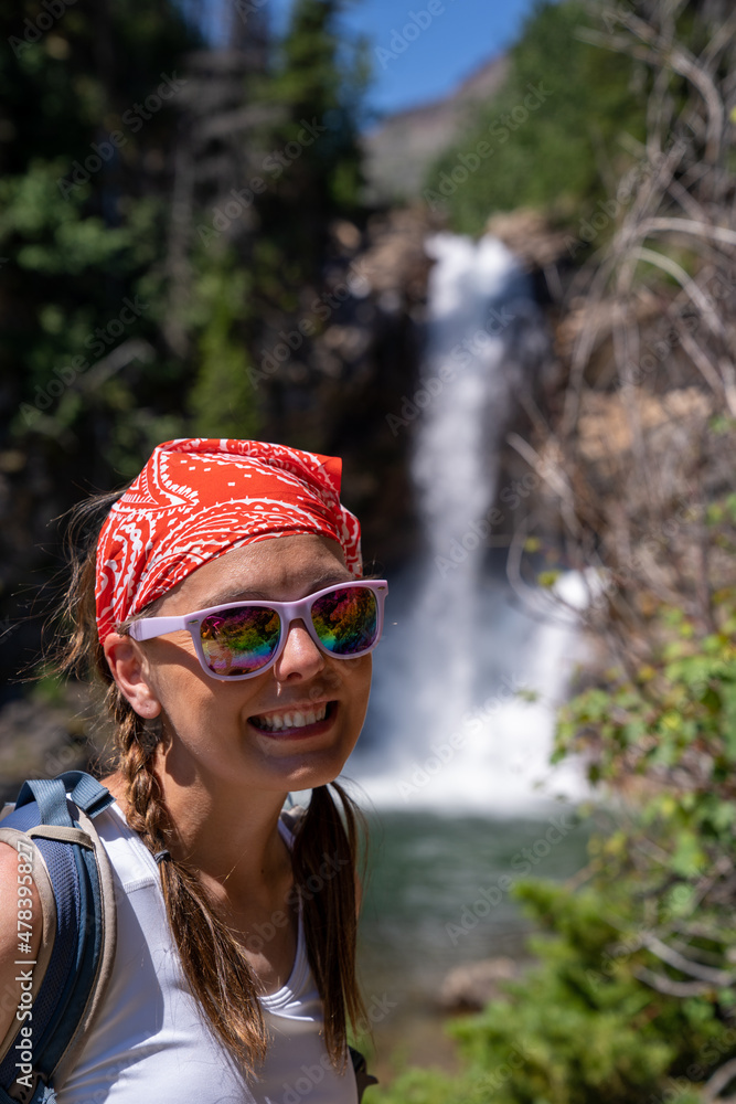Cute woman hiker with braided hair wearing a tank top poses at Running Eagle Falls waterfall in Glacier National Park Cute woman hiker with braided hair wearing a tank top poses at Running Eagle Falls waterfall in Glacier National Park