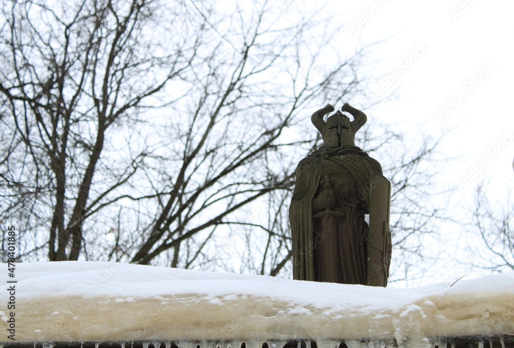 sculpture of a knight in a helmet with horns stands in the snow