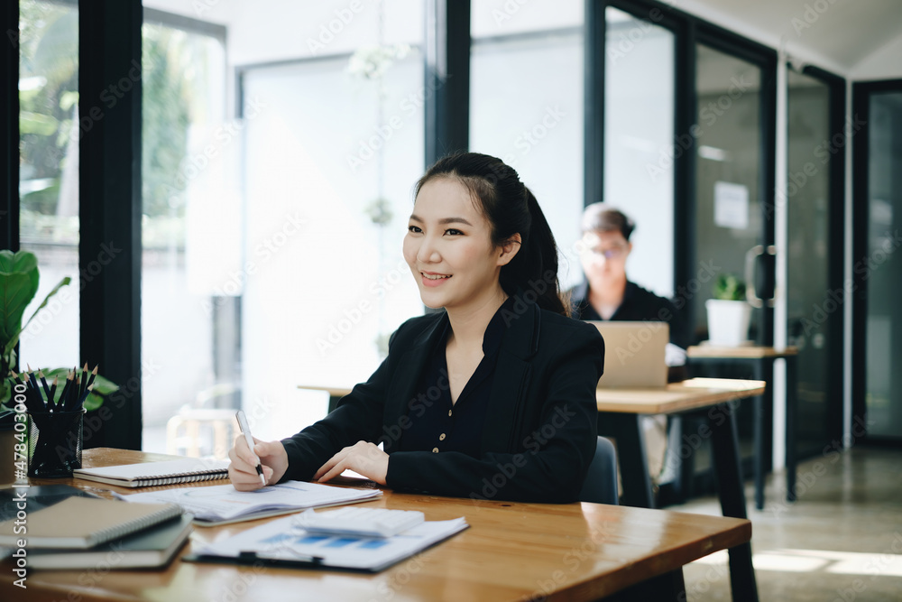 Business woman working to analyze technical price graph and indicator at office with businessman working on background. account or saving money or insurance concept. Business woman working to analyze technical price graph and indicator at office with businessman working on background. account or saving money or insurance concept.