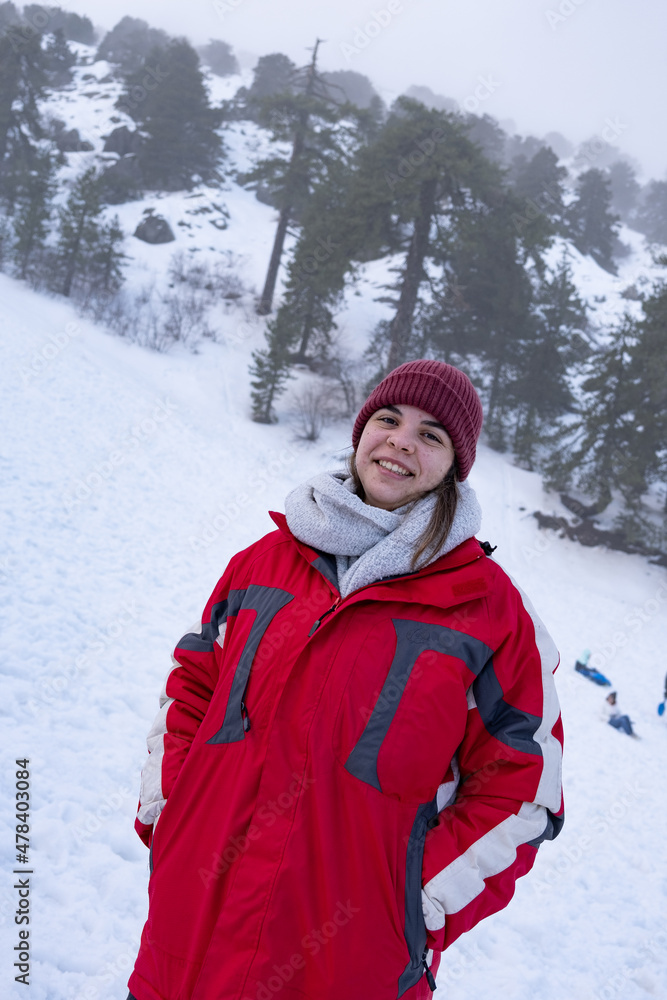 Fototapeta premium Portrait of happy teenage girl smiling and dressed in warm red coat at snow in winter