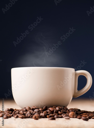 white cup of coffee with smoke on rustic wooden table  with roasted coffee beans  blue background