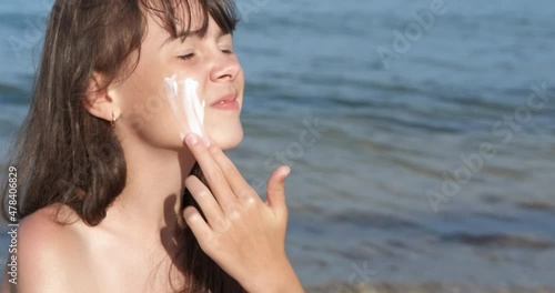 Child face with sunscreen. A happy young girl apply sunblock on her face on the sunny beach. photo