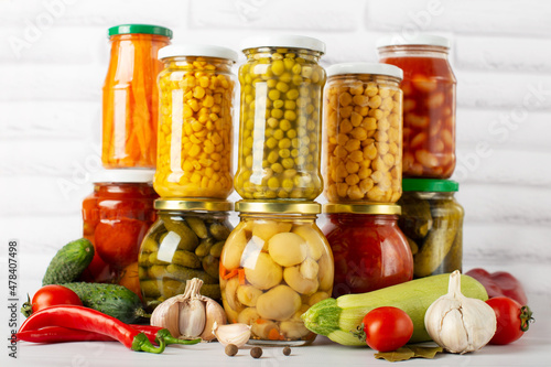 canned food on a white table with vegetables, different types of canned vegetables in glass jars