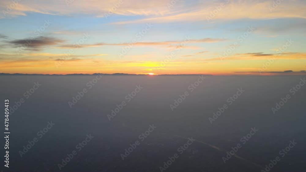 Aerial view of colorful sunset over white dense foggy clouds cover with distant dark silhouettes of mountain hills on horizon Aerial view of colorful sunset over white dense foggy clouds cover with distant dark silhouettes of mountain hills on horizon