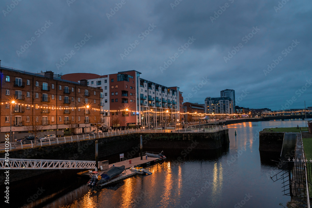 Riverside area at night. Shannon river, Limerick city, Ireland. Blue and orange colors. Dusk scene. Cloudy sky. Christmas and New Year illumination.