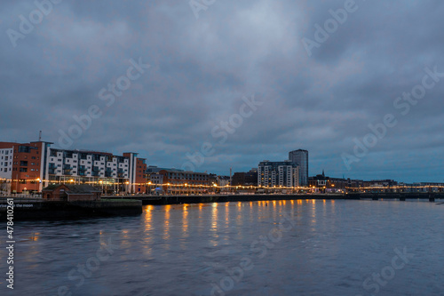 Riverside area at night. Shannon river, Limerick city, Ireland. Blue and orange colors. Dusk scene. Cloudy sky. Christmas and New Year illumination. © mark_gusev