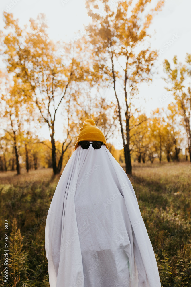 Person dressed as ghost wearing yellow beanie surrounded by trees Person dressed as ghost wearing yellow beanie surrounded by trees