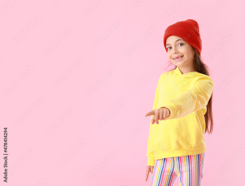 Adorable little girl in yellow hoodie pointing at something on pink background Adorable little girl in yellow hoodie pointing at something on pink background