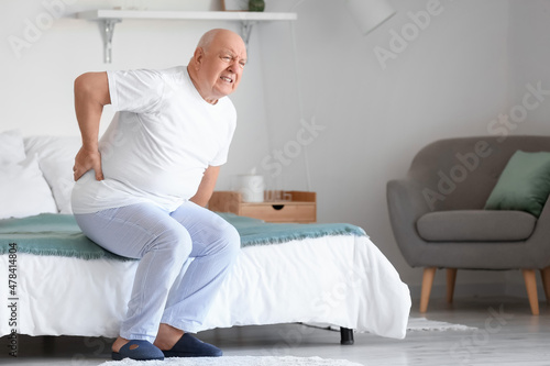 Senior man suffering from back pain on bed at home