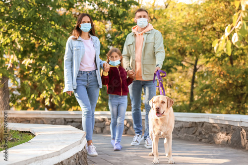 Happy family in medical masks with Labrador dog walking in park