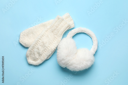 Knitted mittens and earmuffs on color background