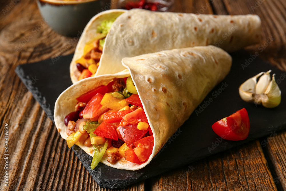 Board of tasty Mexican burritos with vegetables on wooden background, closeup Board of tasty Mexican burritos with vegetables on wooden background, closeup