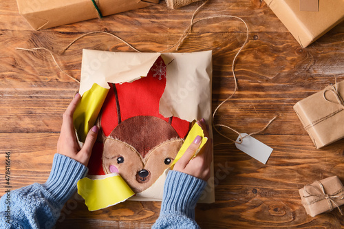 Woman in warm sweater unwrapping Christmas present on wooden background, closeup photo