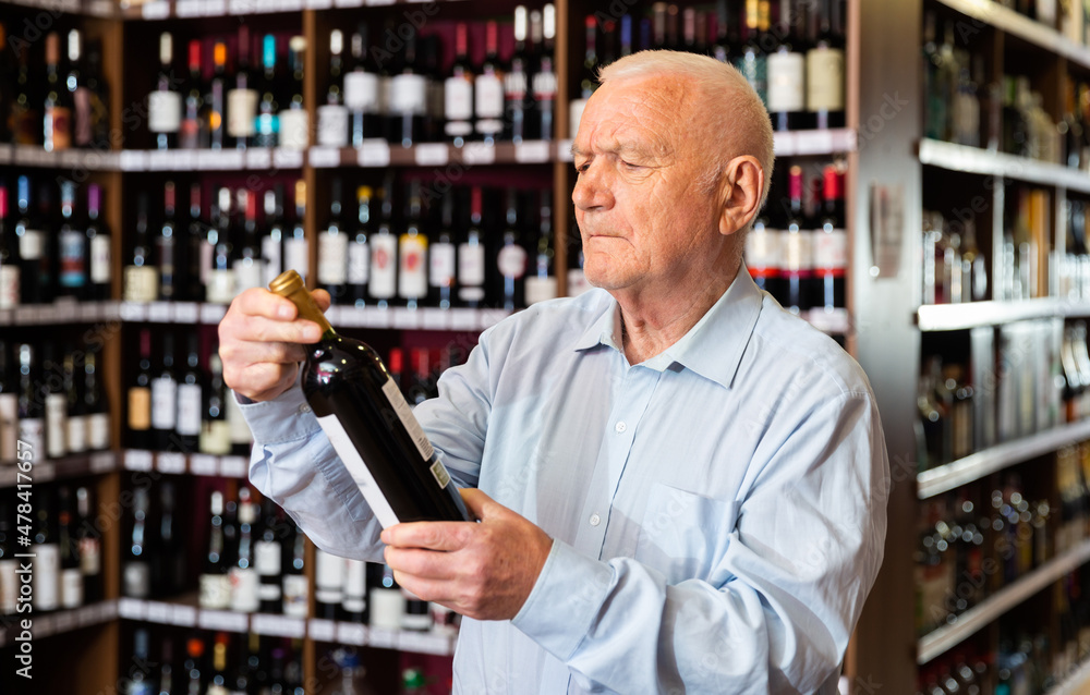 Elderly man chooses red wine in a liquor store. High quality photo