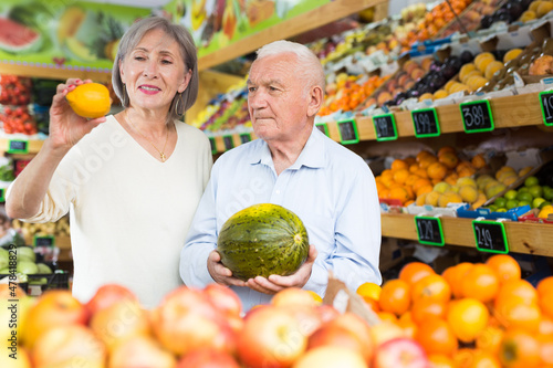 Elderly married couple choosing different fruits together in vegetable supermarket