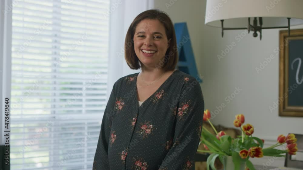 Handheld portrait of pregnant woman holding belly and smiling at camera while standing in home Handheld portrait of pregnant woman holding belly and smiling at camera while standing in home