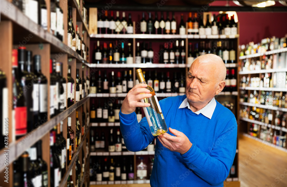 Confident serius pensioner chooses white wine in a liquor store