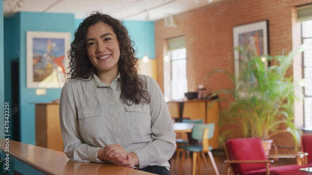 Woman casually smiles at the camera while leaning on desk in an urban building Woman casually smiles at the camera while leaning on desk in an urban building