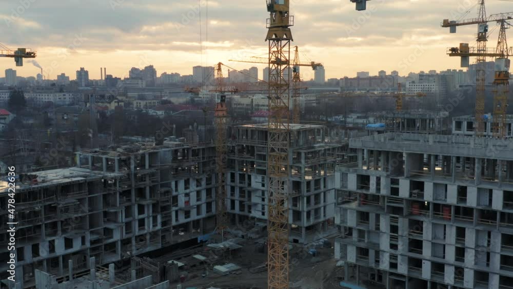 Aerial all-round view of a large construction of a residential area with many multi-storey buildings under construction, a lot of tower cranes, workers, construction equipment at sunset Aerial all-round view of a large construction of a residential area with many multi-storey buildings under construction, a lot of tower cranes, workers, construction equipment at sunset