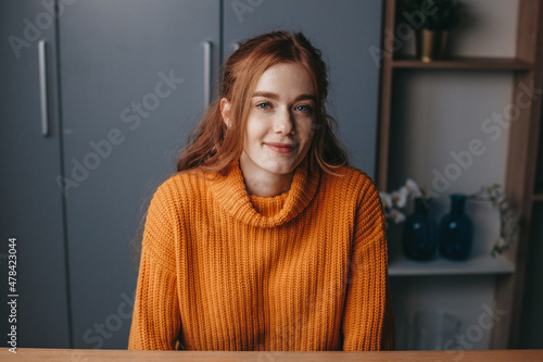 Photo of caucasian redhead woman smiling looking at camera indoor. Freckled face.