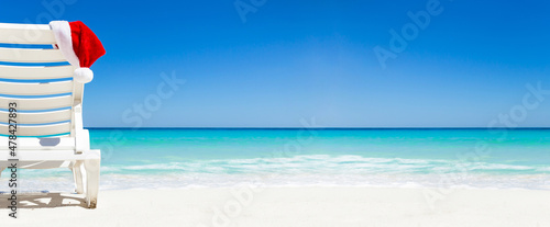 Santa Claus Hat on sunbed near  tropical calm beach with caribbean sea and white sand. Long banner. © photopixel
