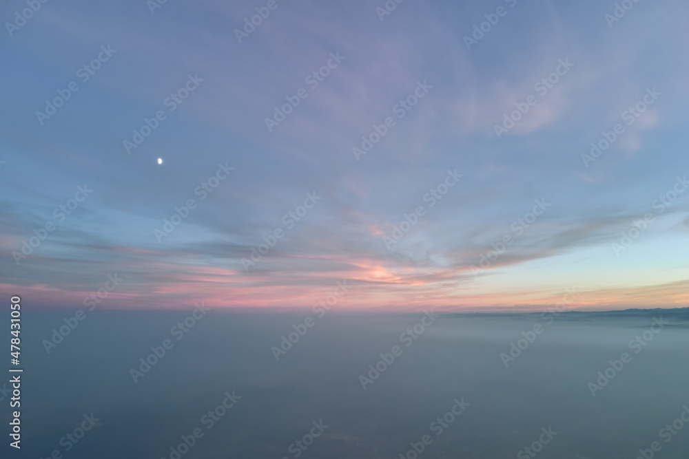 Aerial view of colorful sunset over white dense foggy clouds cover with distant dark silhouettes of mountain hills on horizon Aerial view of colorful sunset over white dense foggy clouds cover with distant dark silhouettes of mountain hills on horizon
