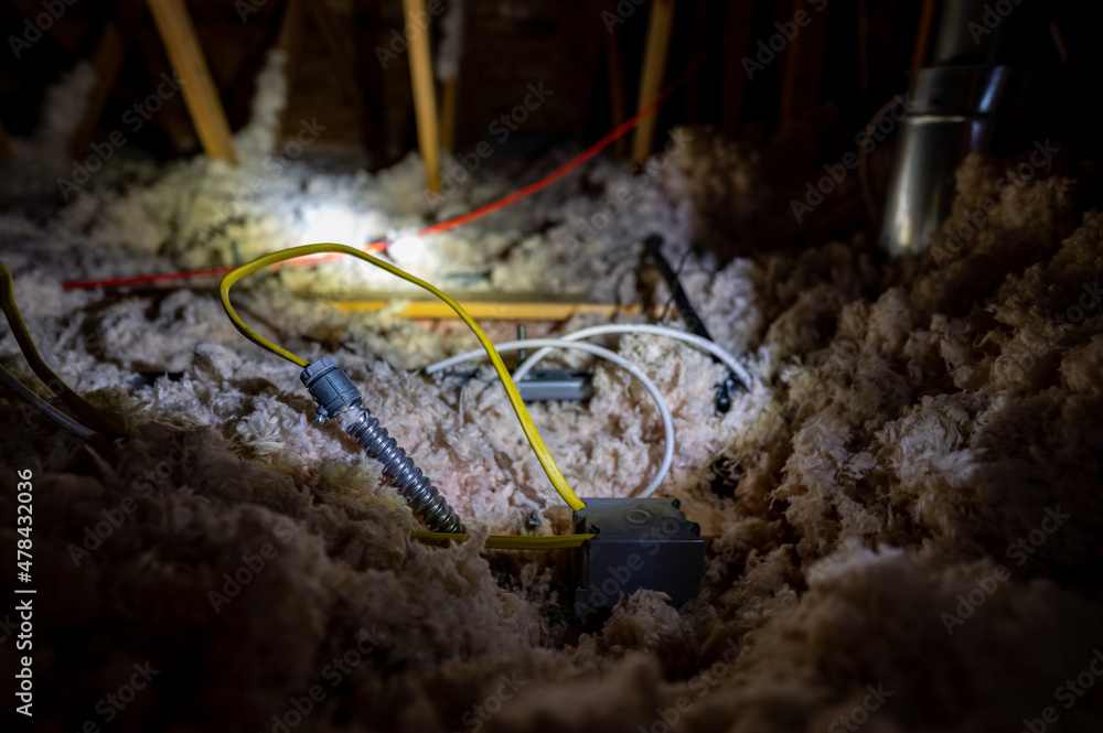 Electrical wire and conduit laying loose on blown insulation in a house attic. 